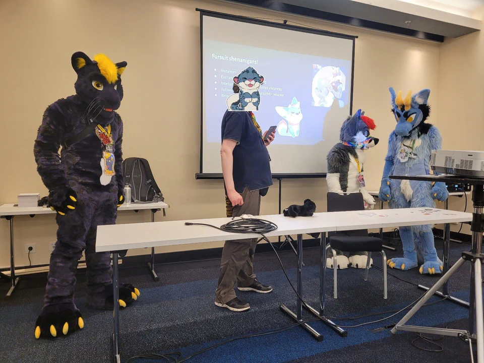 Photo of Finn, myself, Dalite, and NigelDragon standing in front of the presentation screen at the Fediverse panel (picture by Gallen/SequentialSnep)