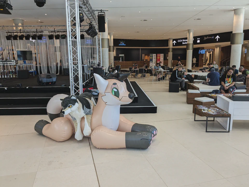 Photo of a large canine plushie sitting on top of an even larger inflatable canine, in front of the open stage in the CCH lobby