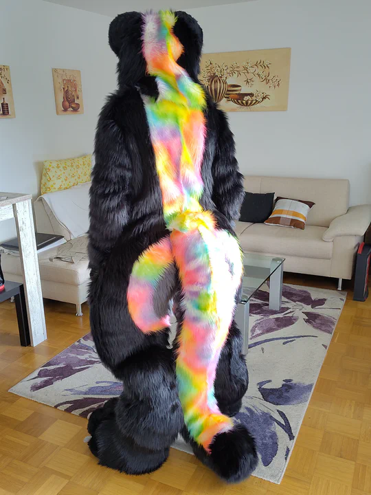 Photo of me wearing my digitigrade fursuit, back view: A large rainbow stripe flows down from the mane along the back and into the tail.

